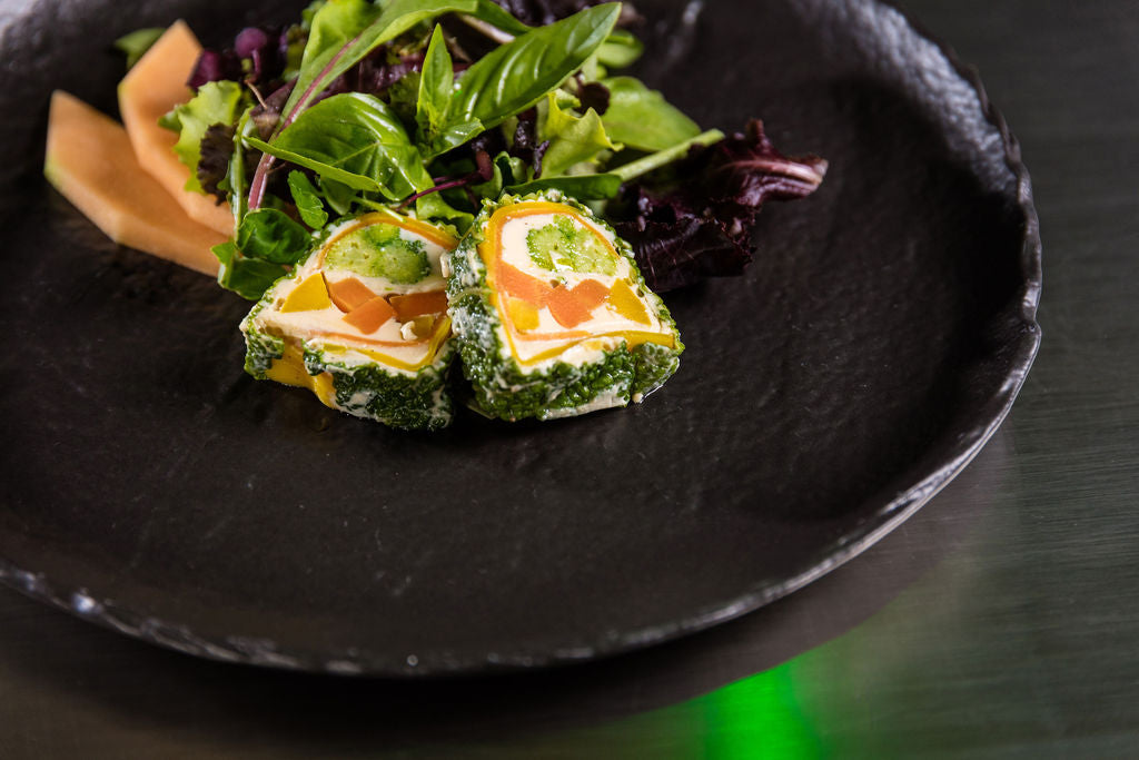 Gemüse-Terrine von Degusta Manufaktur auf schwarzem Teller mit Blattsalat, Melone und Basilikum