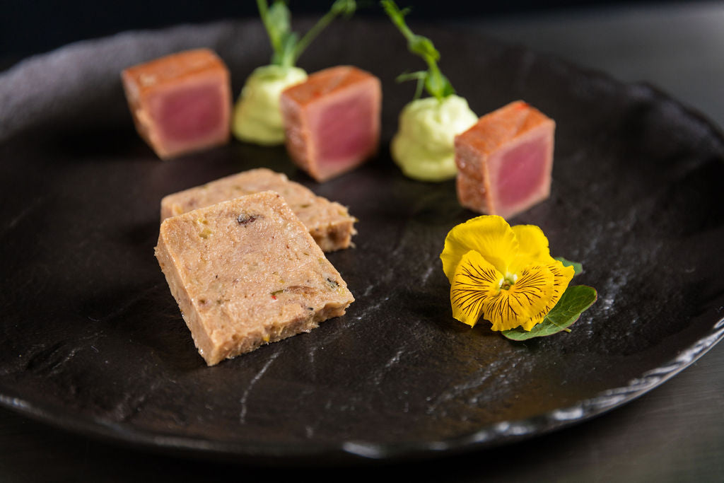 Kalbfleisch-Terrine von Degusta Manufaktur auf schwarzer Schieferplatte mit Avocadocreme und Essblüte