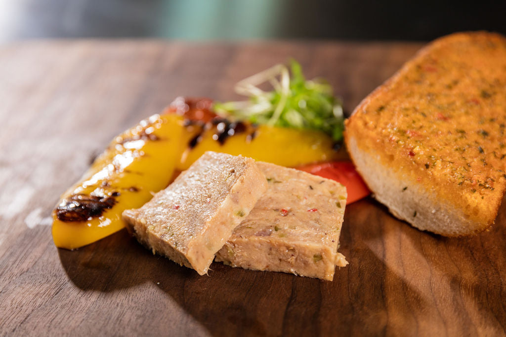 Kalbfleisch-Terrine von Degusta Manufaktur auf Holzbrett mit grilliertem Peperoni und Knoblauchbrot