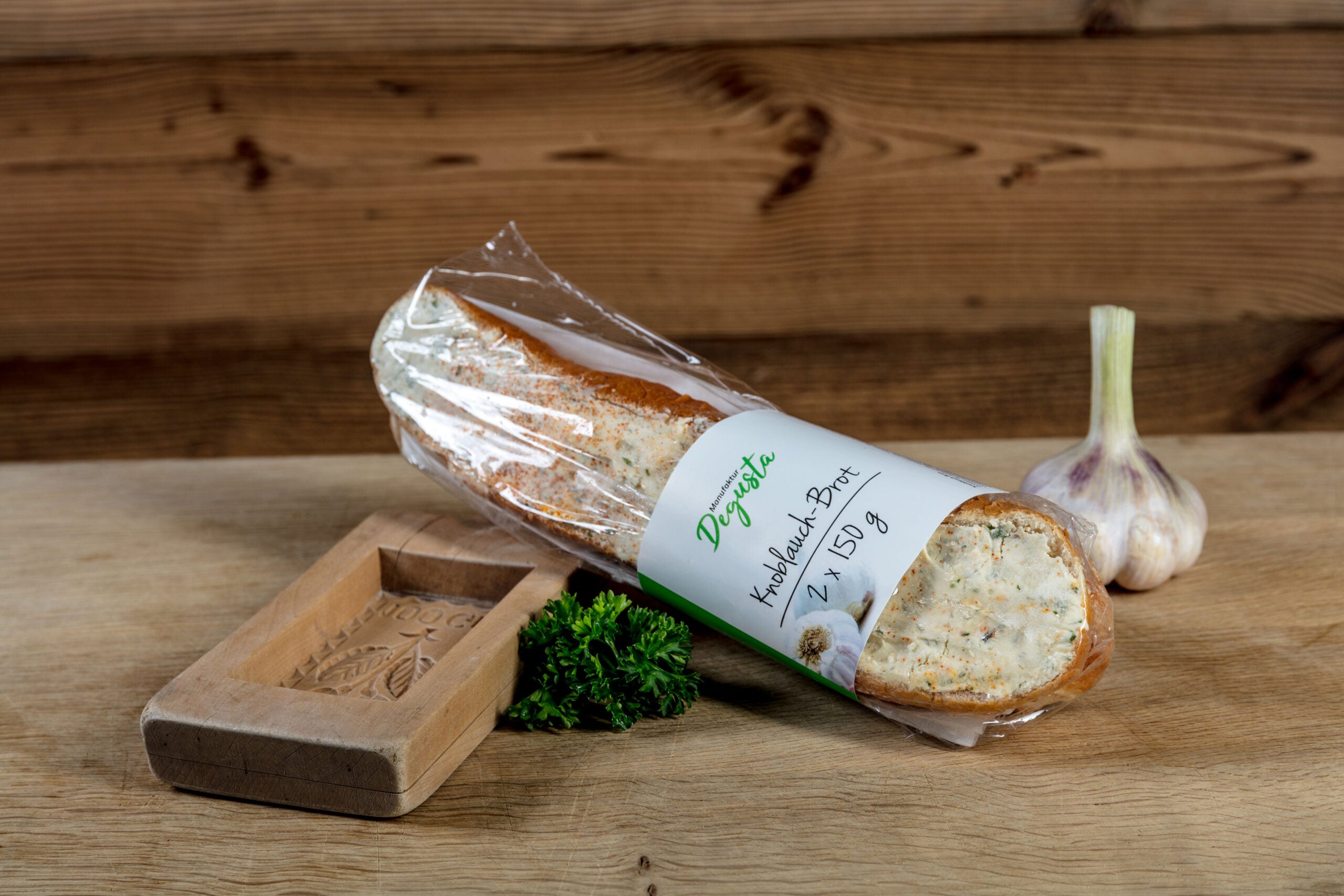 Knoblauch-Brot Classic von Degusta Manufaktur in der Verpackung, dazu Knoblauch und Petersilie