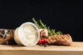 Limetten-Basilikum-Butter von Degusta Manufaktur im hellen Becher, daneben Knoblauch, Rosmarin und ein grilliertes Steak